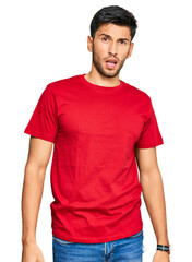 Obraz premium Young handsome man wearing casual red tshirt in shock face, looking skeptical and sarcastic, surprised with open mouth