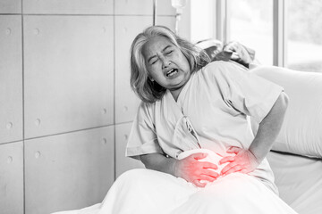 Asian elderly woman has a stomachache, severe abdominal pain, She sat on the bed, The concept of...