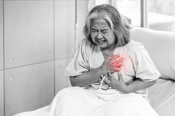 Asian senior old woman sitting on bed suffering from sudden heart attack and hold chest. Concept of...