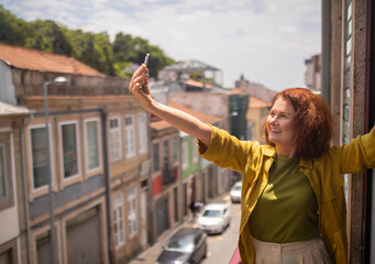Joyful senior woman stretching out her arm and taking selfie on balcony