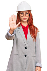 Young redhead woman wearing architect hardhat doing stop sing with palm of the hand. warning expression with negative and serious gesture on the face.