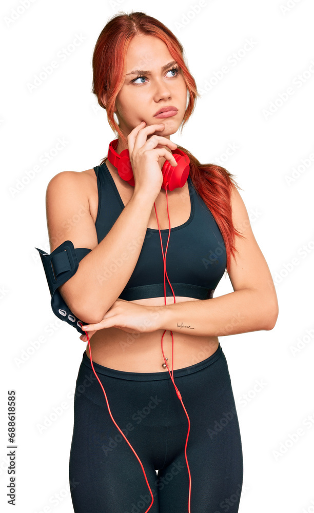 Canvas Prints Young redhead woman wearing gym clothes and using headphones serious face thinking about question with hand on chin, thoughtful about confusing idea