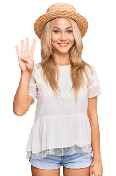 Young blonde girl wearing summer hat showing and pointing up with fingers number four while smiling confident and happy.
