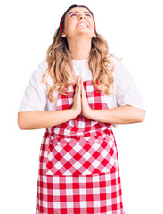 Young caucasian woman wearing apron begging and praying with hands together with hope expression on face very emotional and worried. begging.