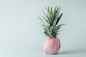 Creative fruit concept. Pineapple wrapped in pink polka dot gift paper on blue pastel background.