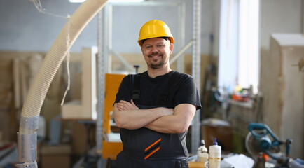 Portrait of young attractive man in work clothes and yellow helmet crossed arms smiling at shop for...