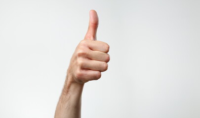 A male hand on a gray background holds a thumb up finger expressing the agreement OK concept is large closeup