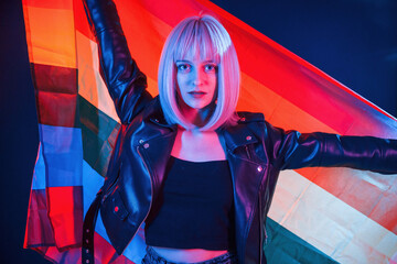 Holding LGBT flag. Woman with white hair is in studio with neon colors