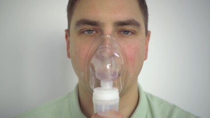 A young man breathes through an inhaler closeup. A man with an oxygen mask is being treated for a...