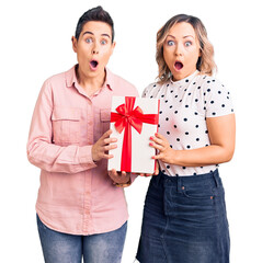 Couple of women holding gift scared and amazed with open mouth for surprise, disbelief face