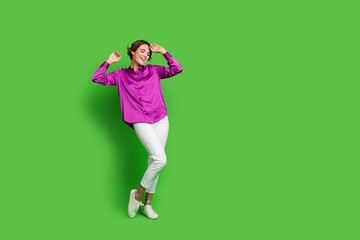 Full length photo of adorable positive carefree lady dressed trendy purple clothes dancing empty space isolated on green color background