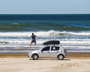 homem em cima de carro na beira da praia do Cassino, em Rio Grande, Rio grande do Sul - obrazy, fototapety, plakaty