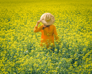 Fototapeta premium mulher de costas não identificada vestida de amarelo com chapéu em campo de canola