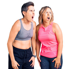 Couple of women wearing sportswear angry and mad screaming frustrated and furious, shouting with anger. rage and aggressive concept.