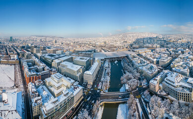 Fototapeta premium Aerial View of Zurich's Central Station Area with Snow-Covered Buildings and Shopping District in December, Sunlit After Snowfall.