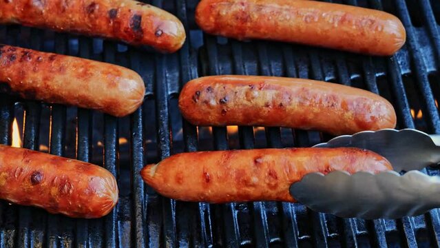 Grilled sausages Bockwurst on barbecue grill grate, flame. Turn the sausages over. Close up. Slow motion.