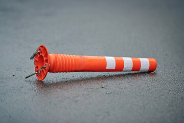Damaged parking post, orange pole lies on the asphalt road. Smashed delineator post in parking lot,...