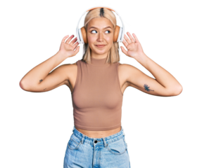 Beautiful young blonde woman listening to music using headphones smiling looking to the side and staring away thinking.