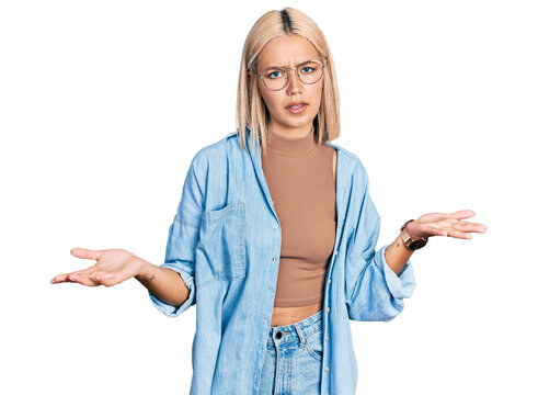 Beautiful young blonde woman wearing glasses clueless and confused with open arms, no idea concept.