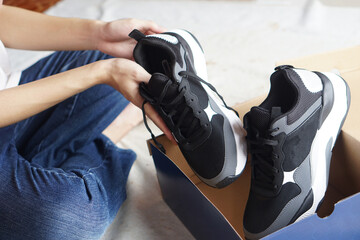 Closeup teenager is holding new sneakers, shoes from package box. Concept, ordering and delivery shoes to home. Checking the quality of product or goods.  - obrazy, fototapety, plakaty