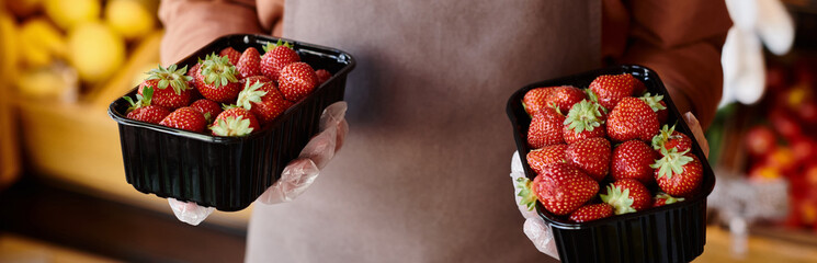 cropped view of mature seller holding two packs of juicy vibrant strawberries in hands, banner