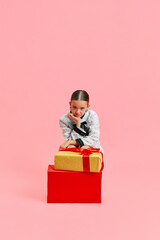 Unpleasant, upset little girl, dressed smart casual outfit sitting near huge gift boxes against...
