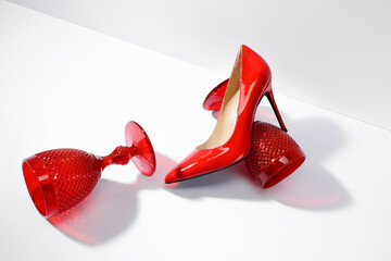 Red glasses and a red women's high-heeled shoe on a white table and background - obrazy, fototapety, plakaty