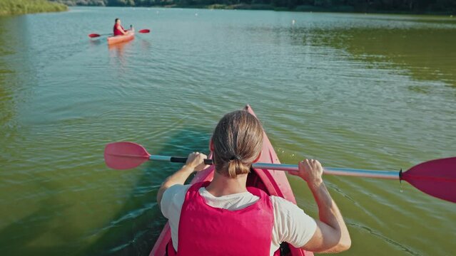 Man wearing red vest while kayaking on lake. Male in canoe paddling oar in middle of calm pond. Guy in boat from back. Woman rowing in kayak nearby. Sport recreation outdoor.