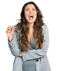 Young hispanic girl wearing business clothes holding glasses angry and mad screaming frustrated and furious, shouting with anger looking up.
