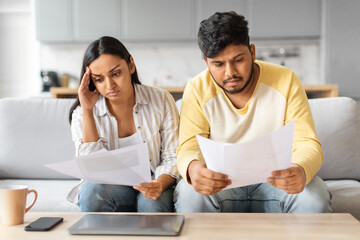 Stressed young indian spouses checking financial papers at home
