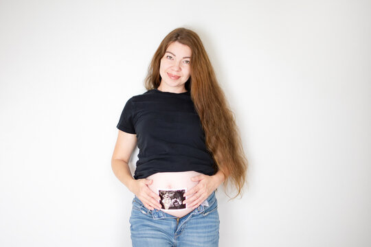 Pregnant Caucasian woman holding ultrasound picture of her baby near baby bump