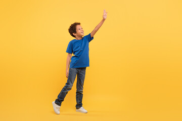 Fototapeta na wymiar Black boy reaching up, blue tee, yellow background