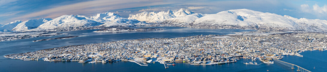 Fototapeta na wymiar Panorama of norwegian city of Tromso in the winter. Snowy roofs, embankment near the port and fishing ships, Sunny winter day.