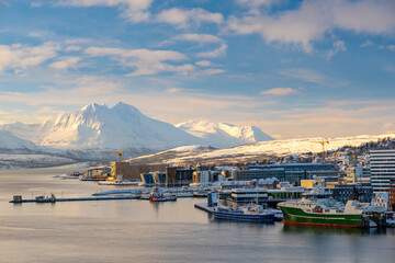 Panorama of norwegian city of Tromso in the winter. Snowy roofs, embankment near the port and fishing ships, Sunny winter day.