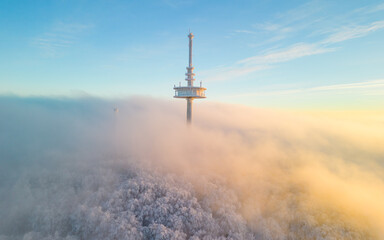 Communication tower on the mountain with the low hanging clouds over the snow covered forest in the...