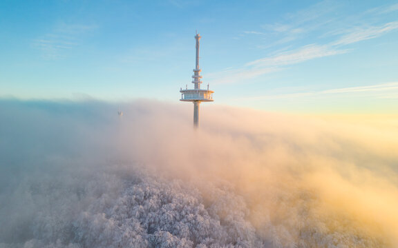 Communication tower on the mountain with the low hanging clouds over the snow covered forest in the beautiful evening light