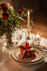 holidays, birthday and celebration concept - close up of festive table serving for two with gift box, flowers in vase and candles burning at home on valentine's day