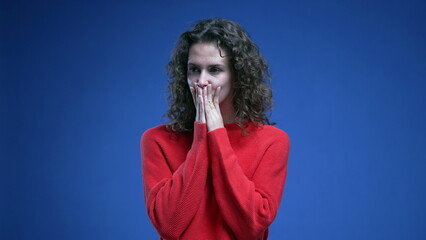 Fototapeta na wymiar Pensive woman struggling with dilemma standing on blue backdrop with red sweater. Thoughtful 20s person during tough decision making