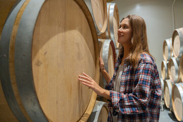 Winery worker woman stand near wine fermentation tank and check the product in modern factory.