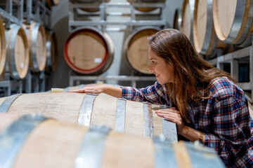 Winery worker woman stand near wine fermentation tank and check the product in modern factory.