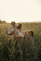 Family portrait on a field in rye in the rays of the setting sun. Father and mother hug their daughters