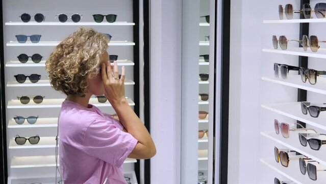 Woman tries fashionable sunglasses from boutique, expressing individuality. Woman confidently chooses sunglasses that will highlight uniqueness. Variety models makes it difficult for woman to choose.