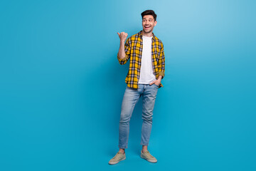 Full body length photo of funny guy wear yellow checkered shirt direct finger empty space with curiosity isolated on blue color background