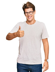 Handsome caucasian man wearing casual clothes and glasses doing happy thumbs up gesture with hand. approving expression looking at the camera showing success.