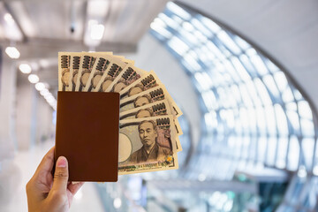 Hand holding a passport with ten thousand Japanese yen bills at the airport. Copy space background