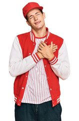 Handsome caucasian man wearing baseball uniform smiling with hands on chest with closed eyes and grateful gesture on face. health concept.