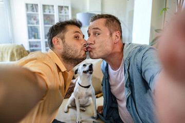 Gay couple taking a selfie for Valentine's Day while kissing. Their dog is looking at them