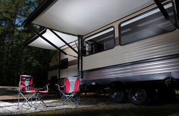 RV ready for glamping in the forest with its awning open and red chairs underneath