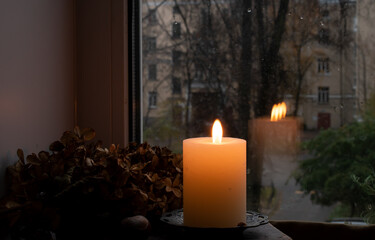 Autumn still life with a candle, a dried hydrangea branch on the background of a window with an urban landscape.