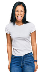 Beautiful hispanic woman wearing casual white tshirt sticking tongue out happy with funny expression. emotion concept.